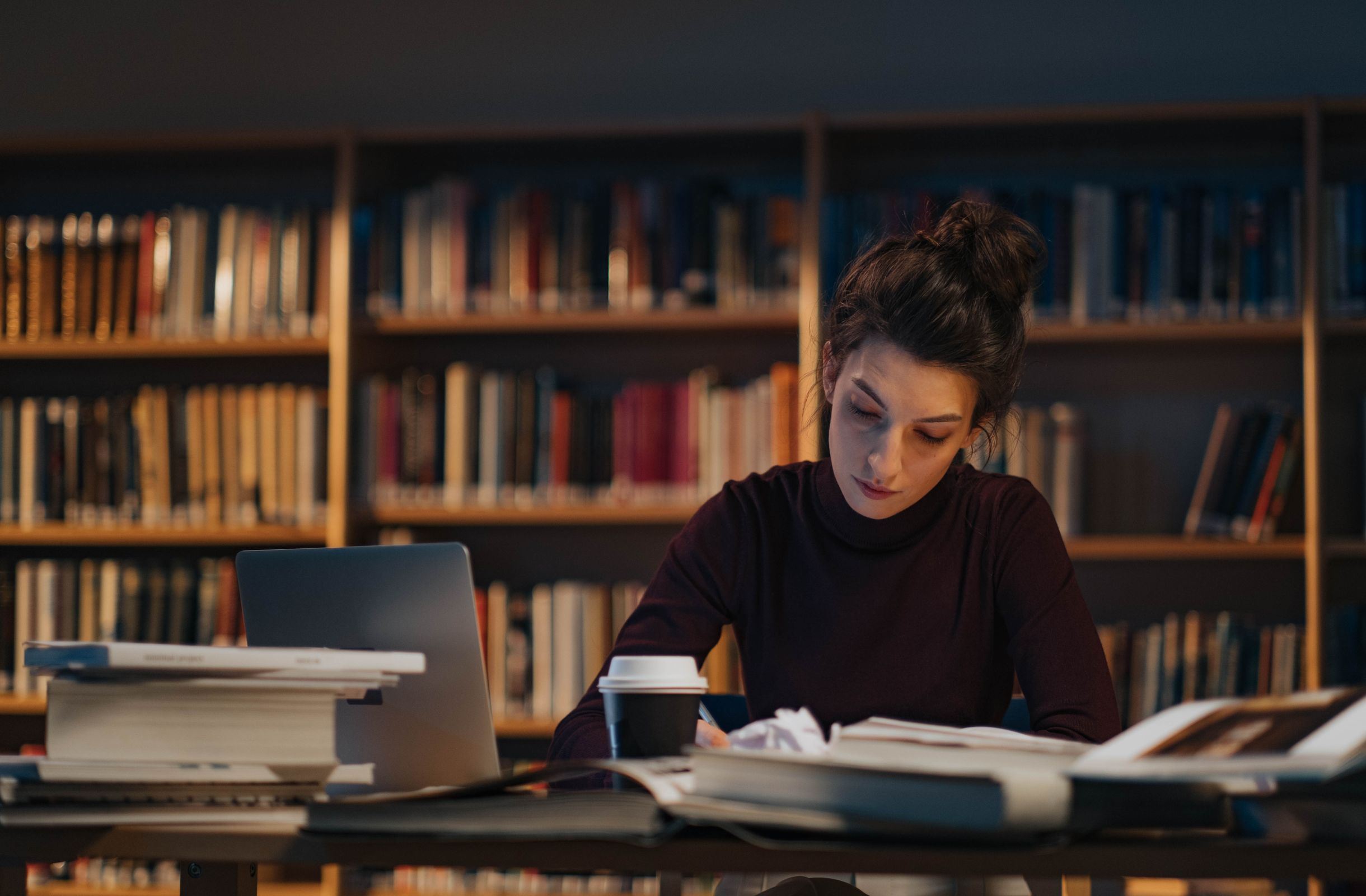 Woman studying in a library with books and a laptop